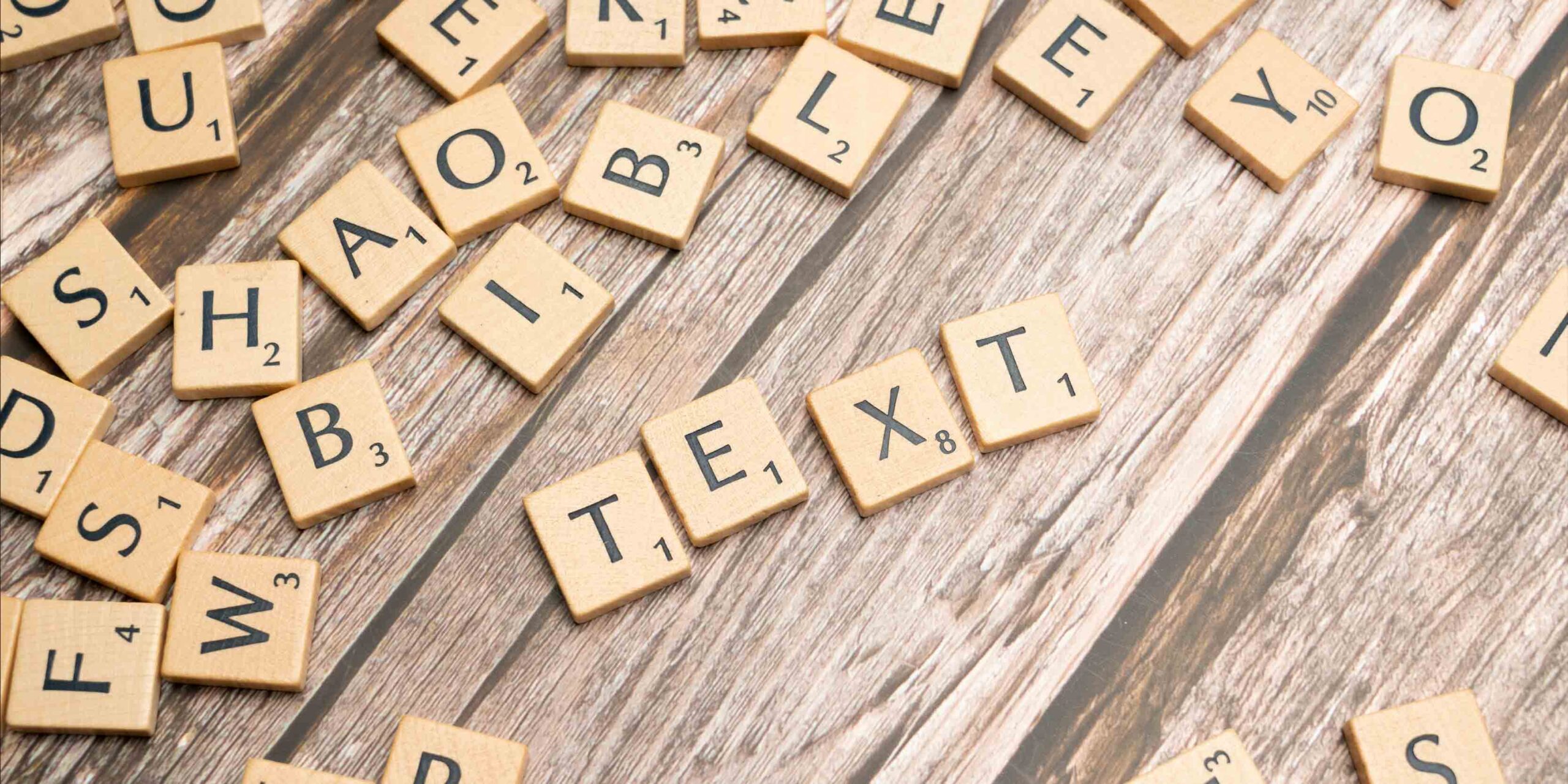 Piezas de Scrabble sobre una mesa de madera, con la palabra "TEXT" formada en el centro